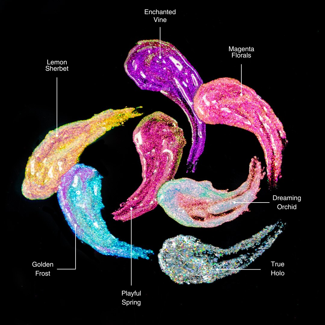 Seven lip gloss shades in green, pink, purple, magenta, gold, and iridescent are arranged side by side and shimmer.