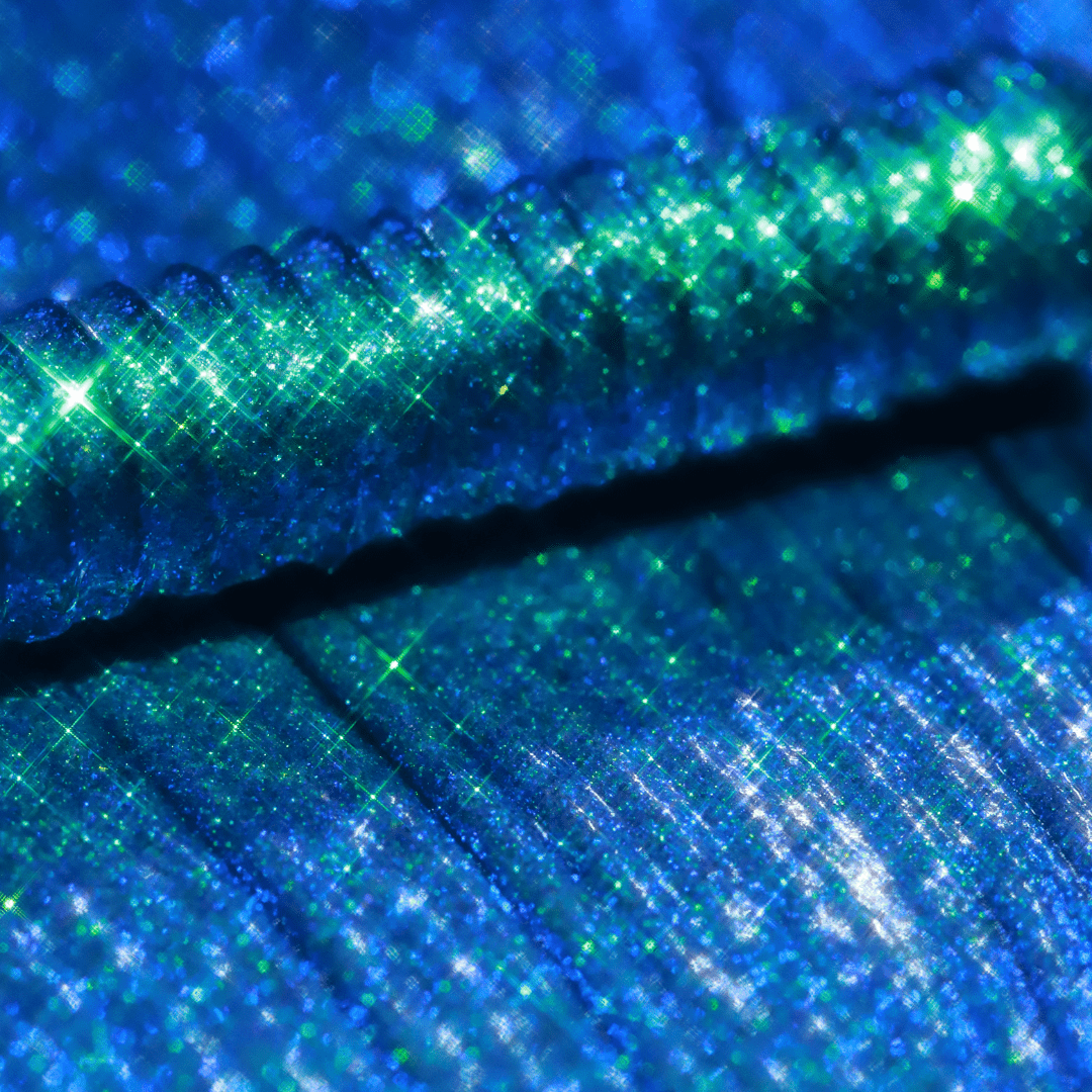 Close-up of a mascara topper with turquoise and green shimmering reflections.