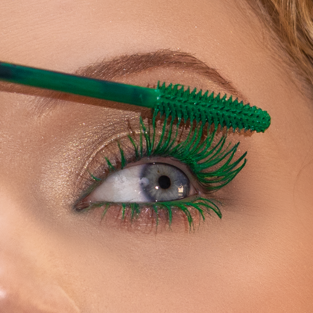 A close-up shows upper eyelashes being coated with green mascara using a green wand.