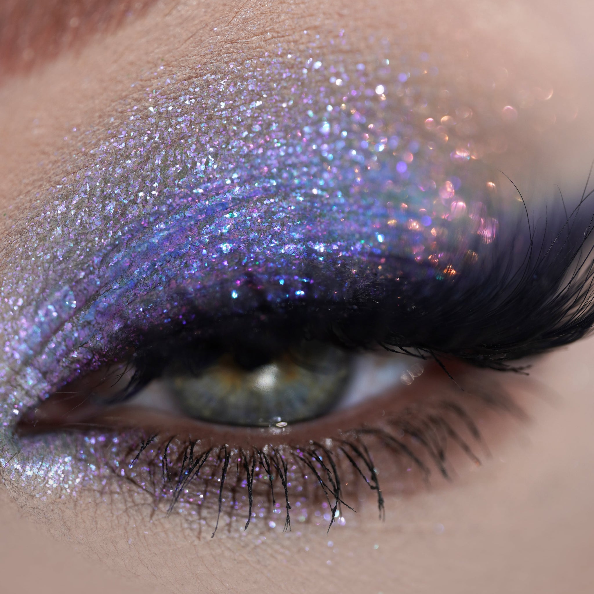 Close-up of an eye with shimmering lavender glitter eyeshadow and long, thick false eyelashes.
