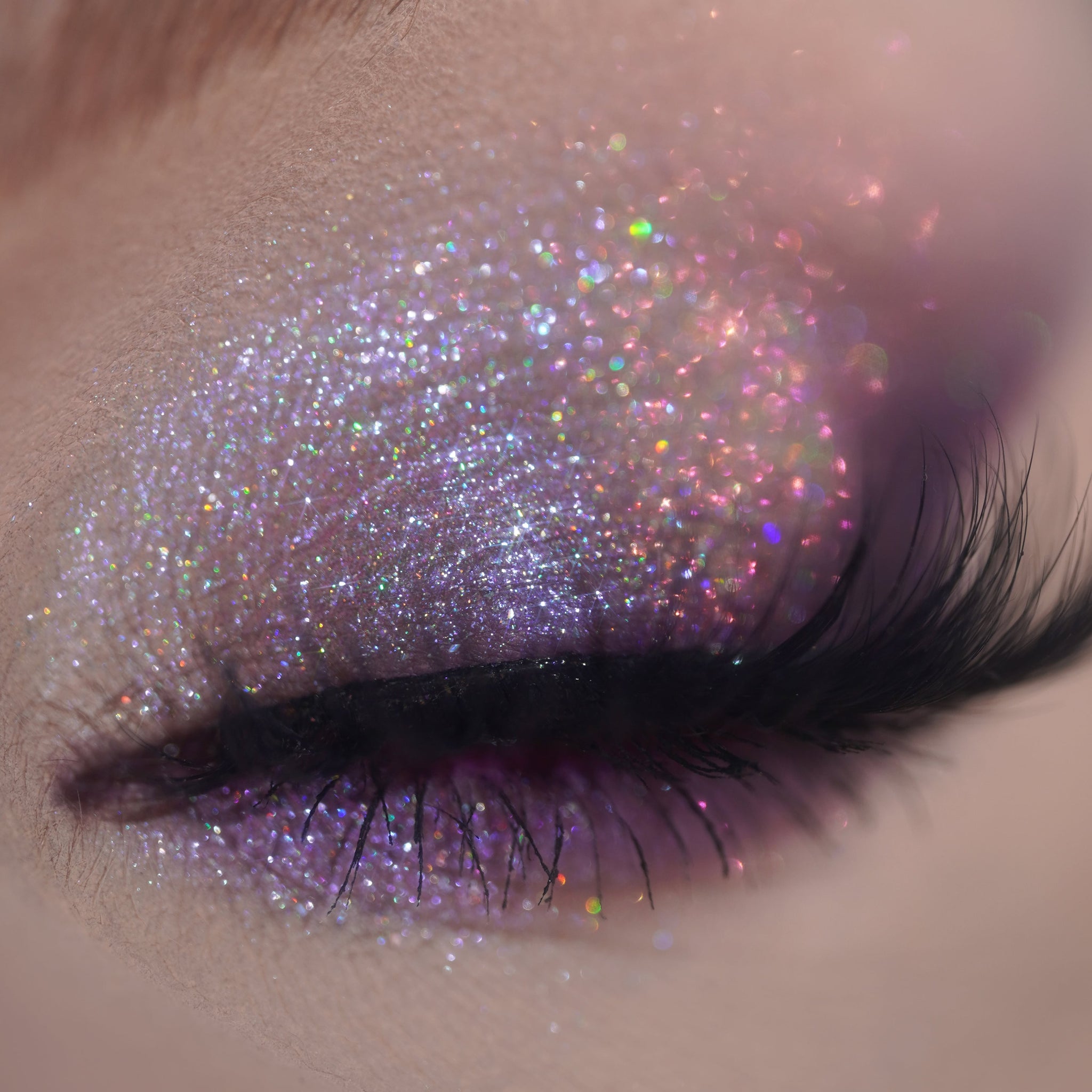 Person with long lashes wears shimmering multicolored glitter eyeshadow.