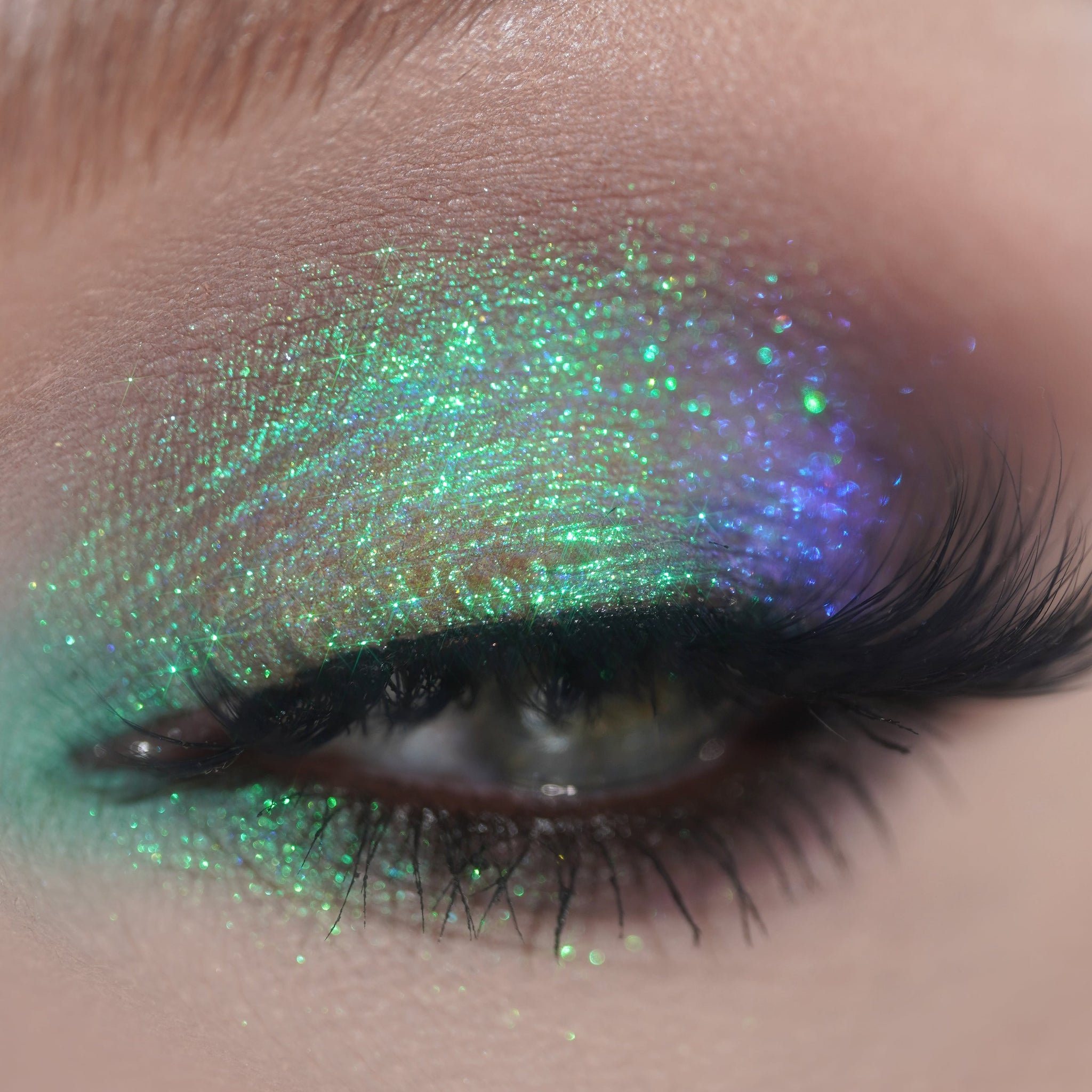 Close-up of an eye with shimmering green and blue eyeshadow and long curled lashes.