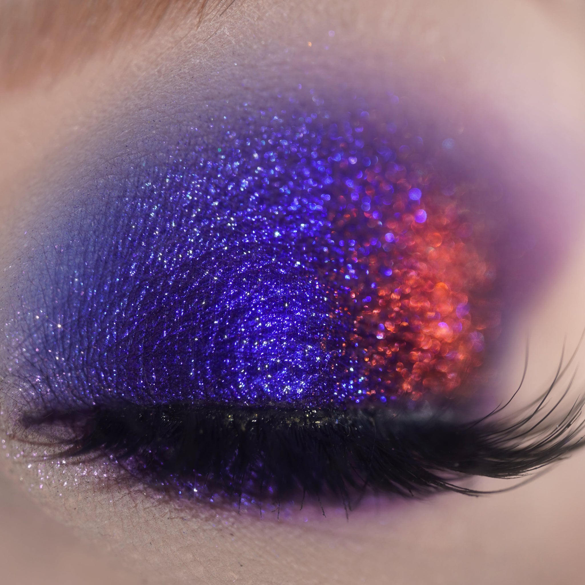Close-up of a closed eye with glittery blue and red eyeshadow and long black false lashes.