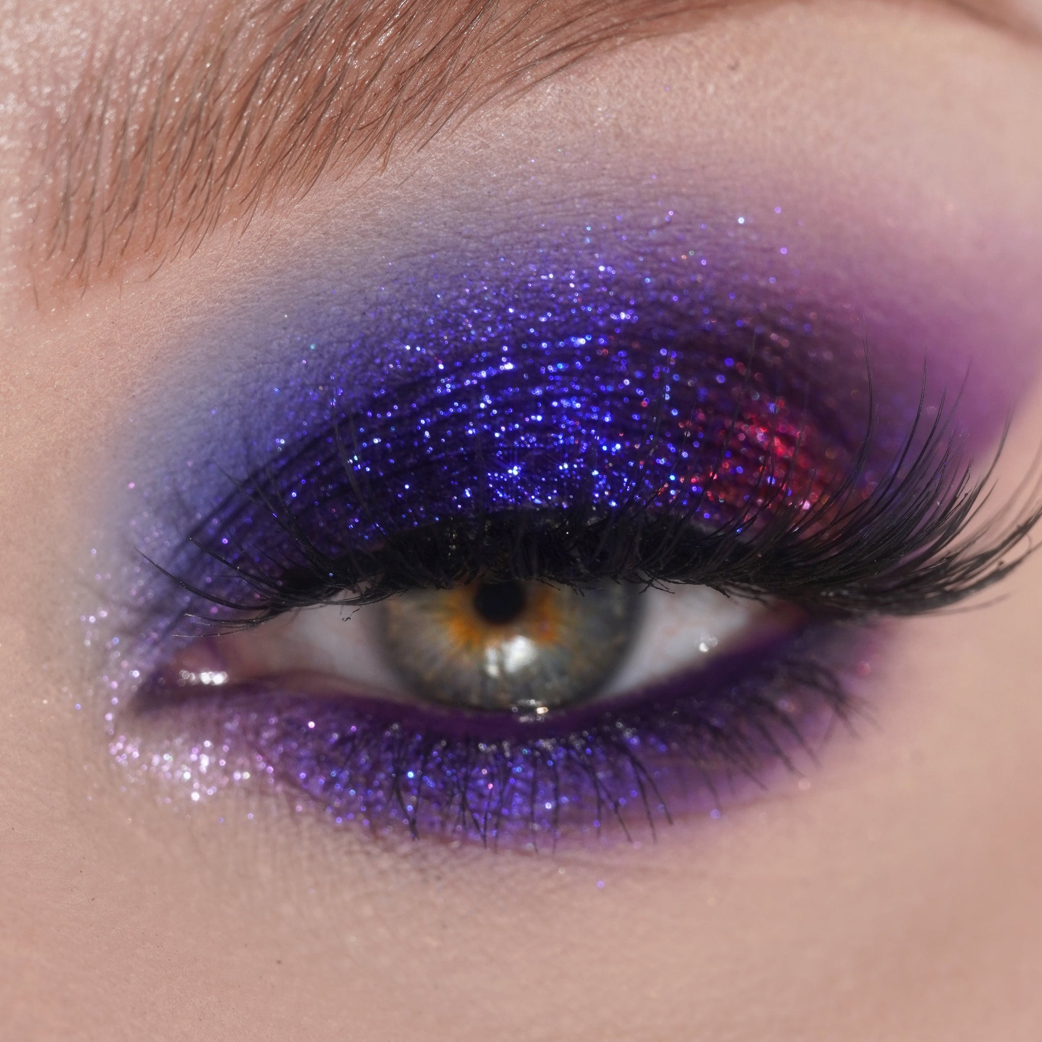 Close-up of an eye with bold red and blue glitter eyeshadow and long eyelashes.