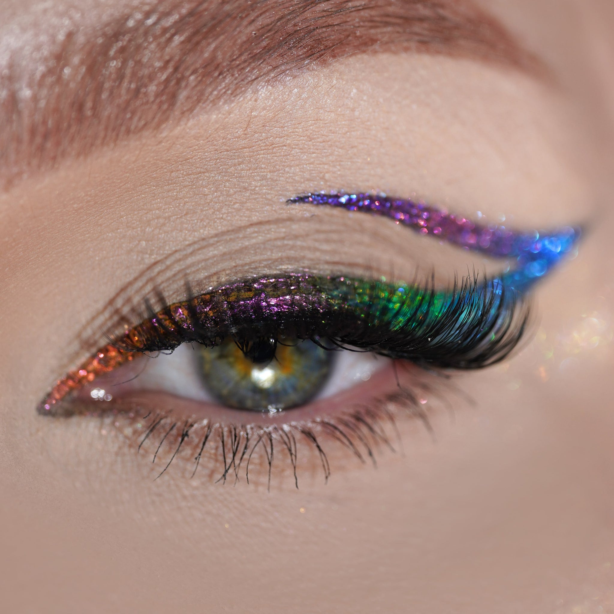 Close-up of an eye with rainbow eyeliner and false lashes, featuring shimmery color above the eyelid.