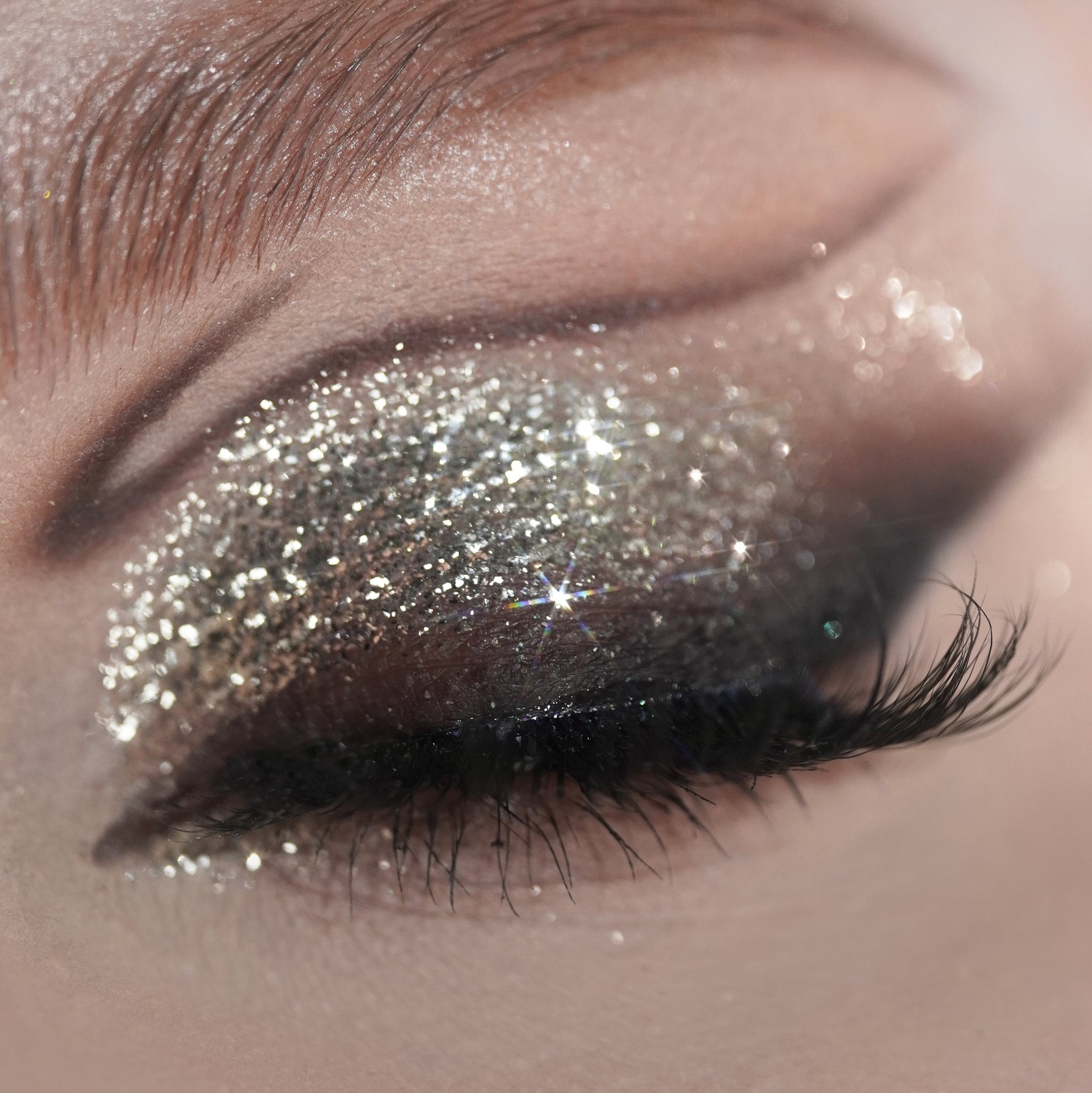 Closed eye with silver glitter eyeshadow and long thick lashes