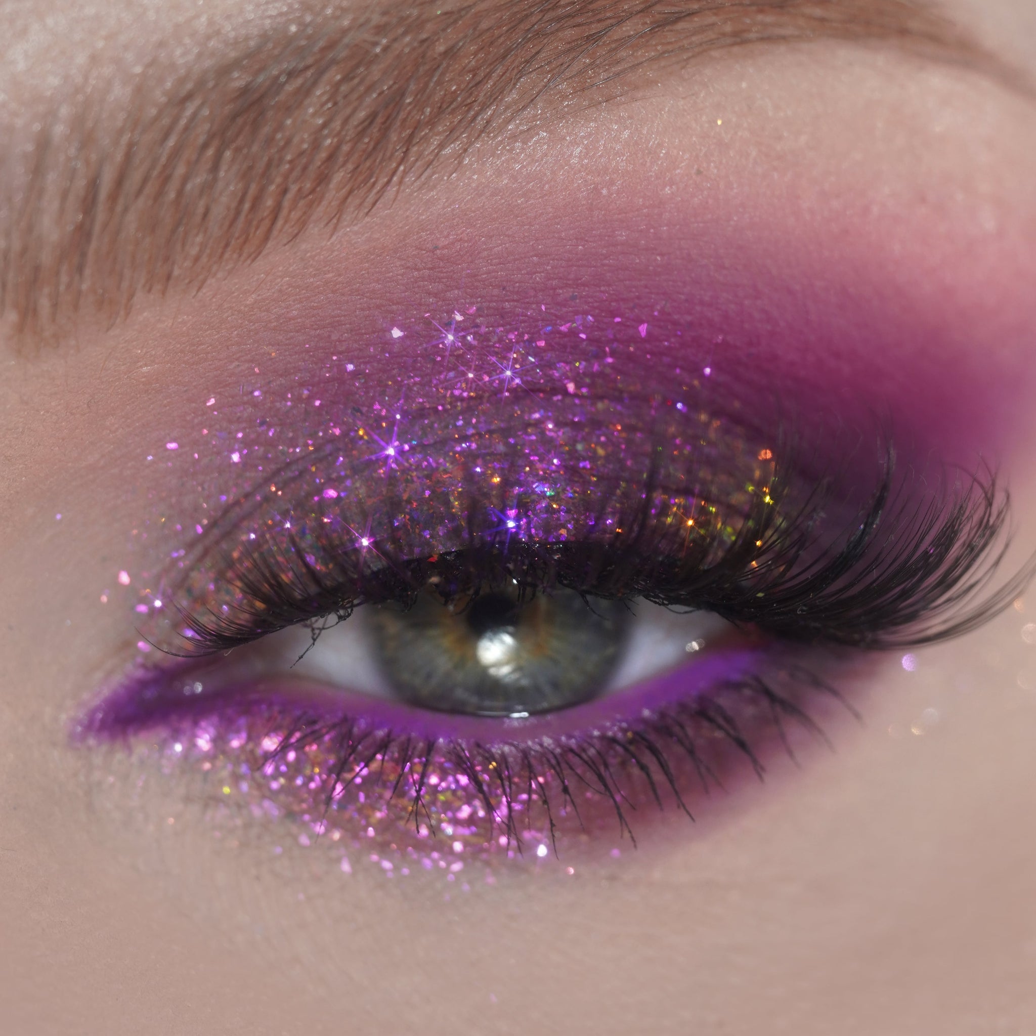 Close-up of an eye with pink and purple glitter eyeshadow and long, defined eyelashes.