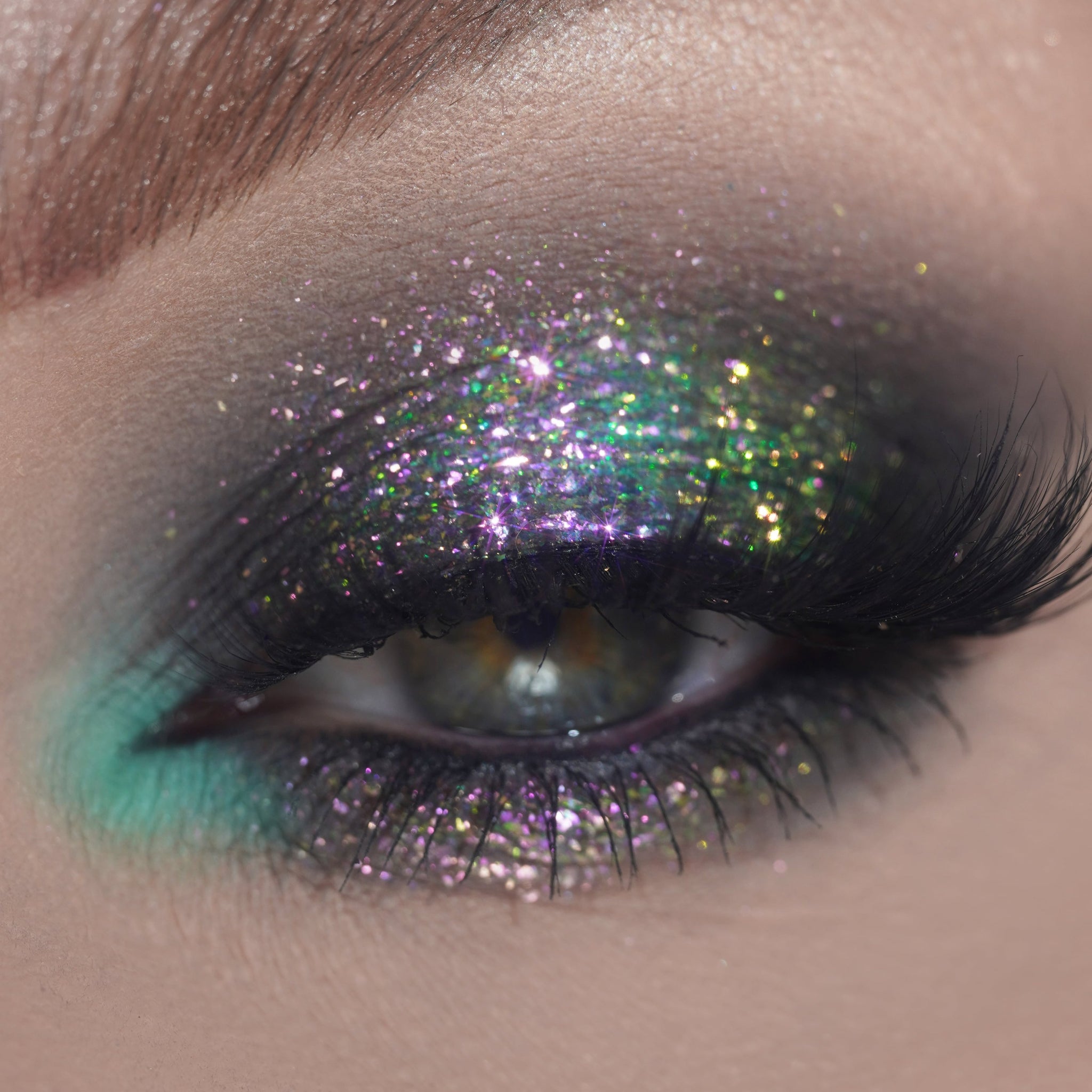 Close-up of an eye with glittery purple and green eyeshadow and long black lashes.