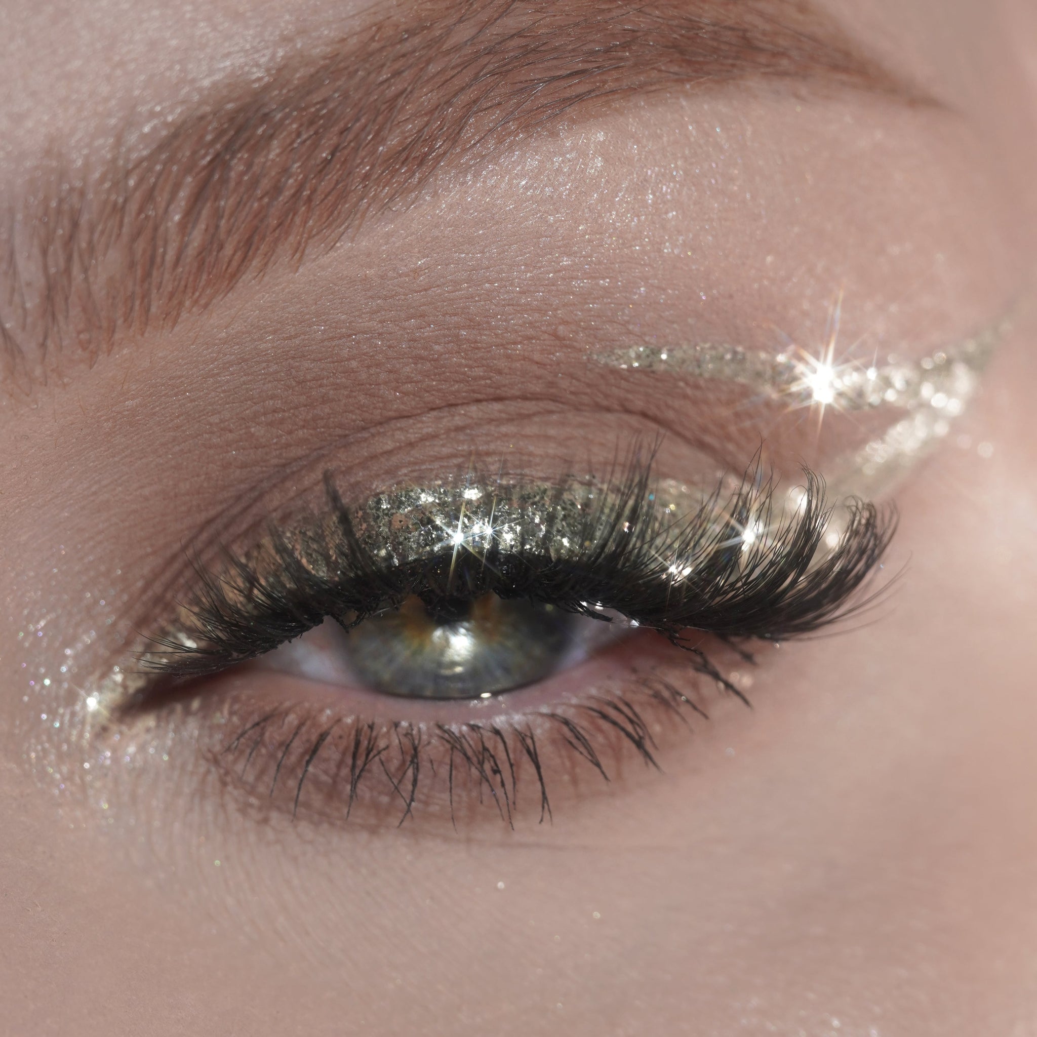 Close-up of an eye with silver glitter eyeliner and long thick lashes.