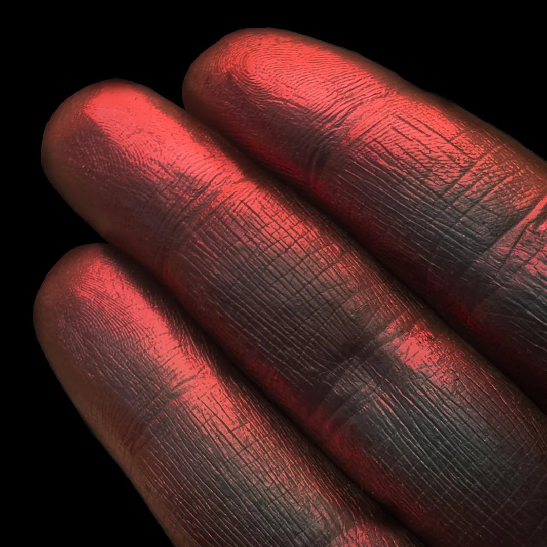 Three fingers display shimmery red pigment against a solid black background.