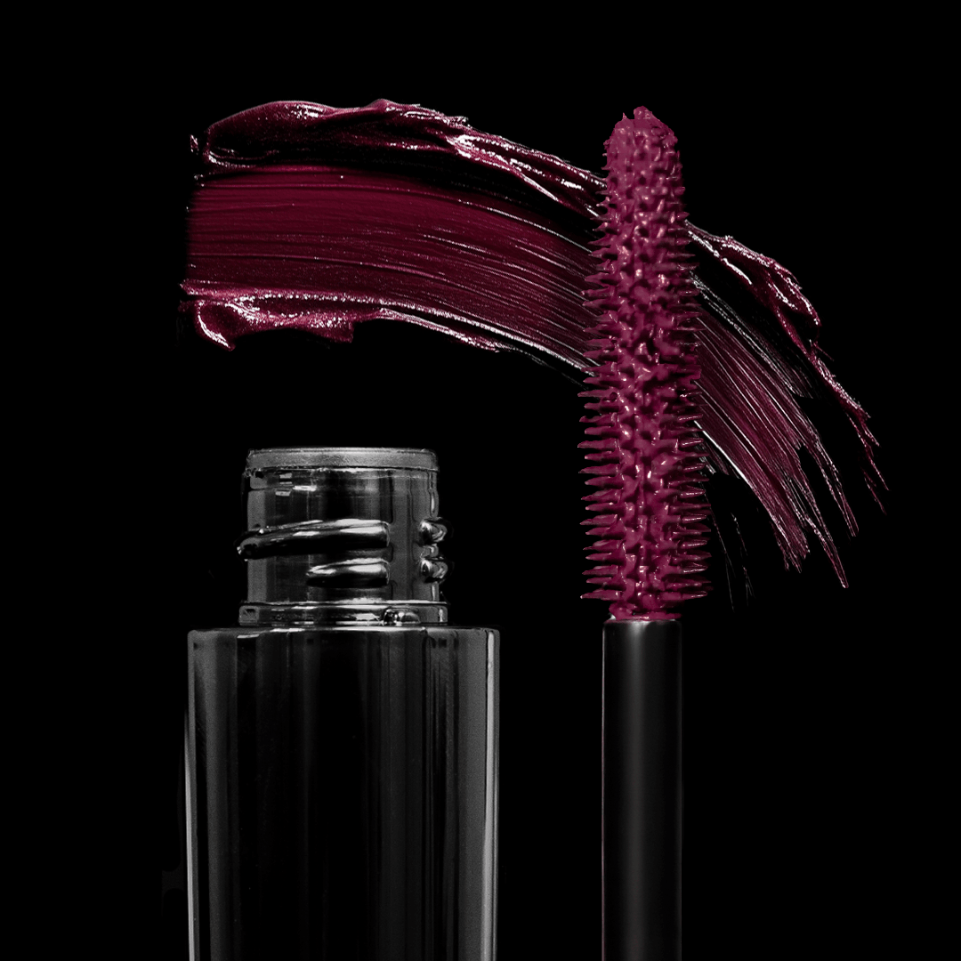 A burgundy mascara tube and brush with a bold swipe of color are displayed on a black background.