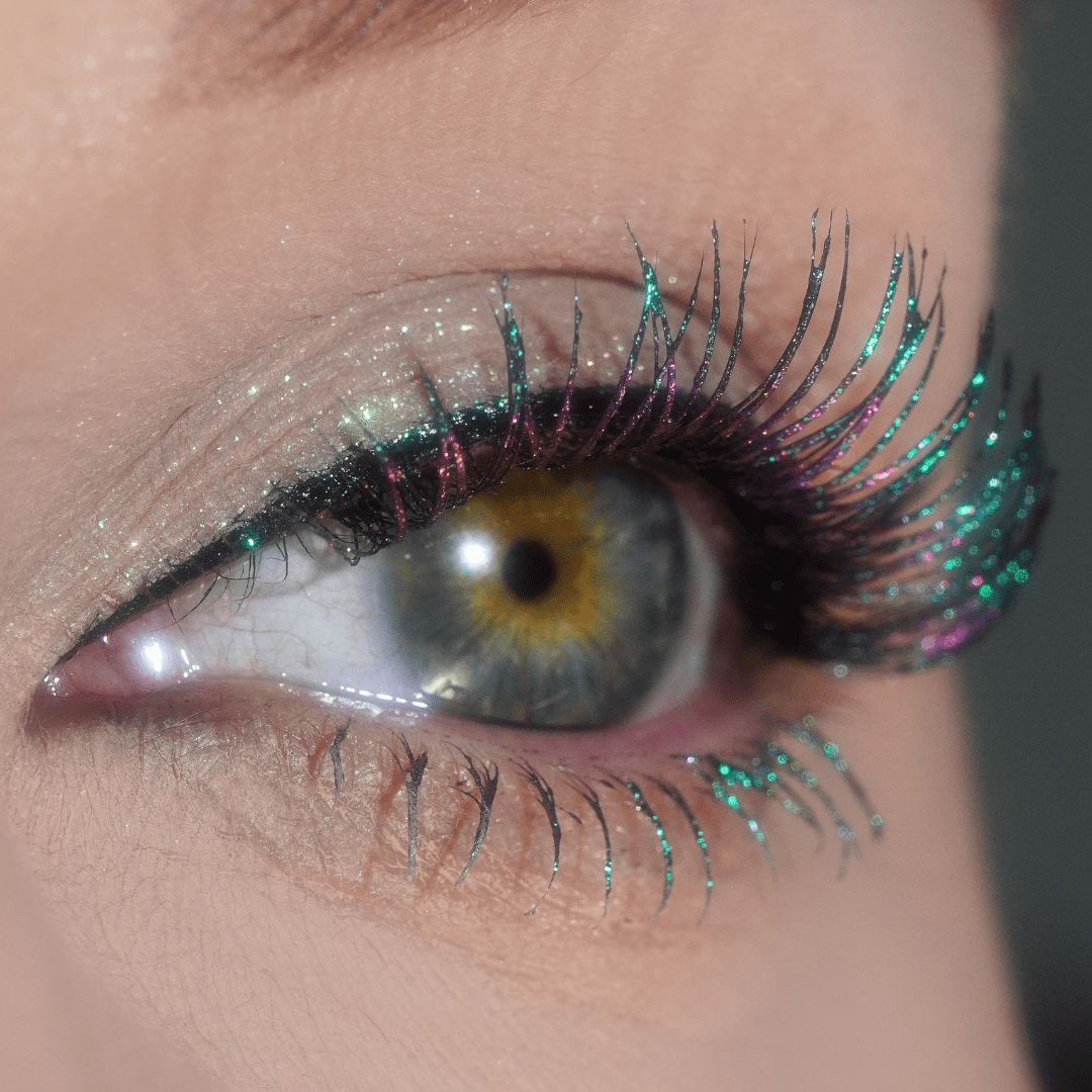 Close-up of an eye with long green and purple sparkly lashes