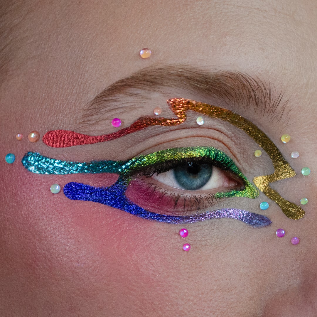 Close-up of an eye with bold, colorful makeup and small shimmering Water Droplet Gems above the eyelid.