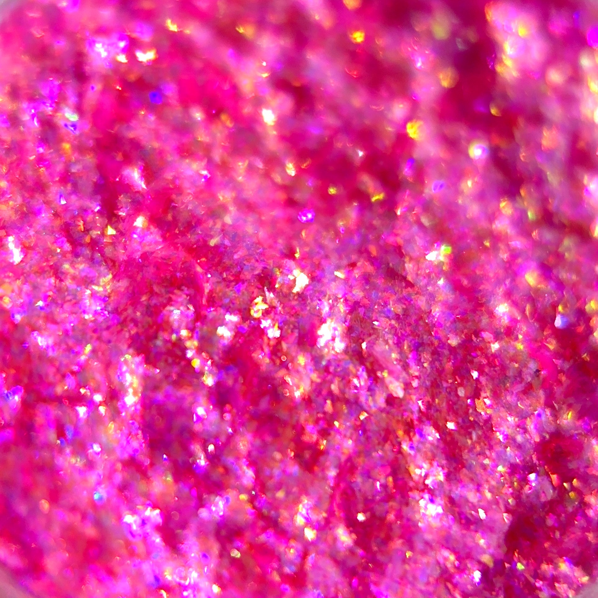 Close-up of an iridescent pink surface with gold, purple, and orange glitter flecks.