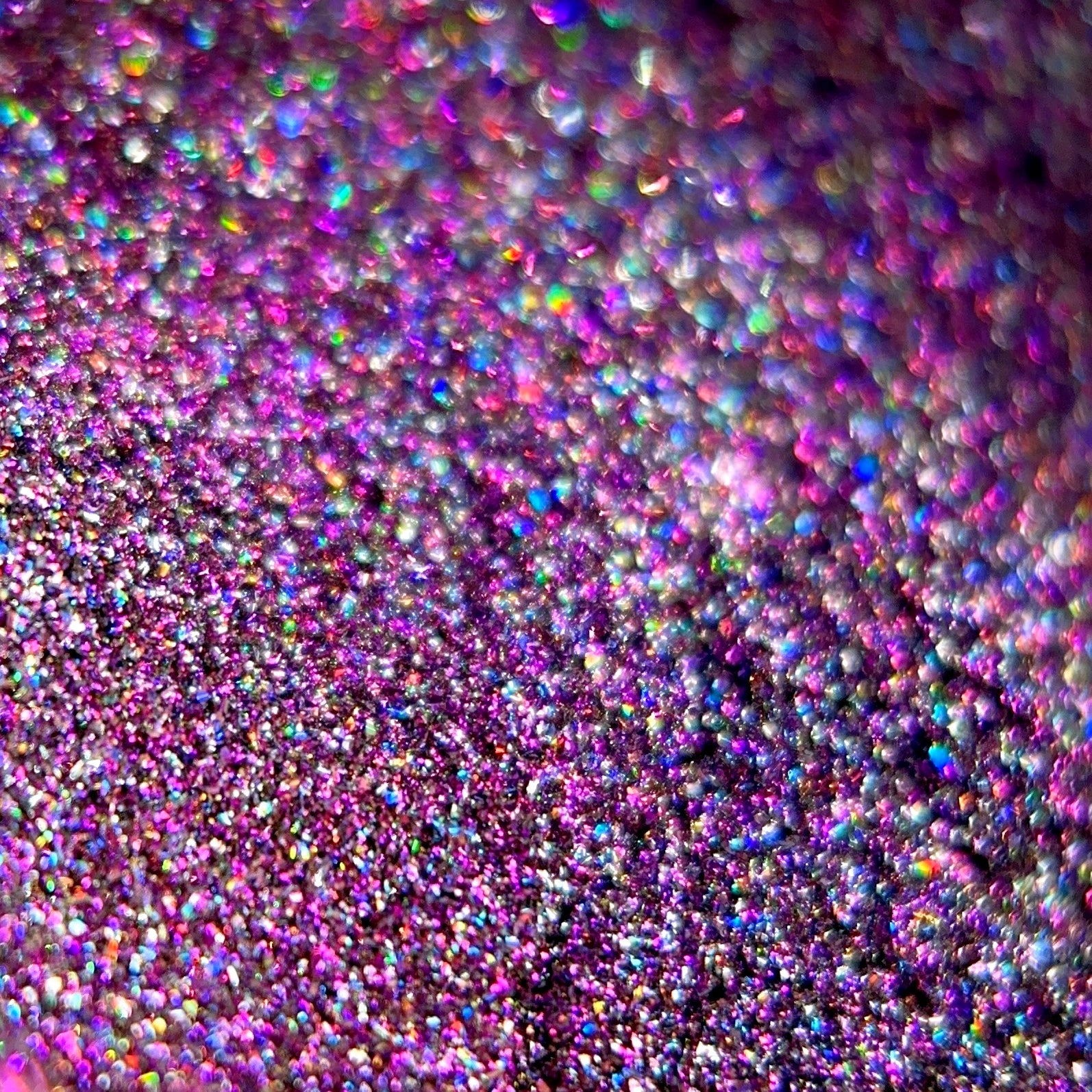 Close-up of holographic glitter in pink, purple, and rainbow colors with a shimmering blurred texture.