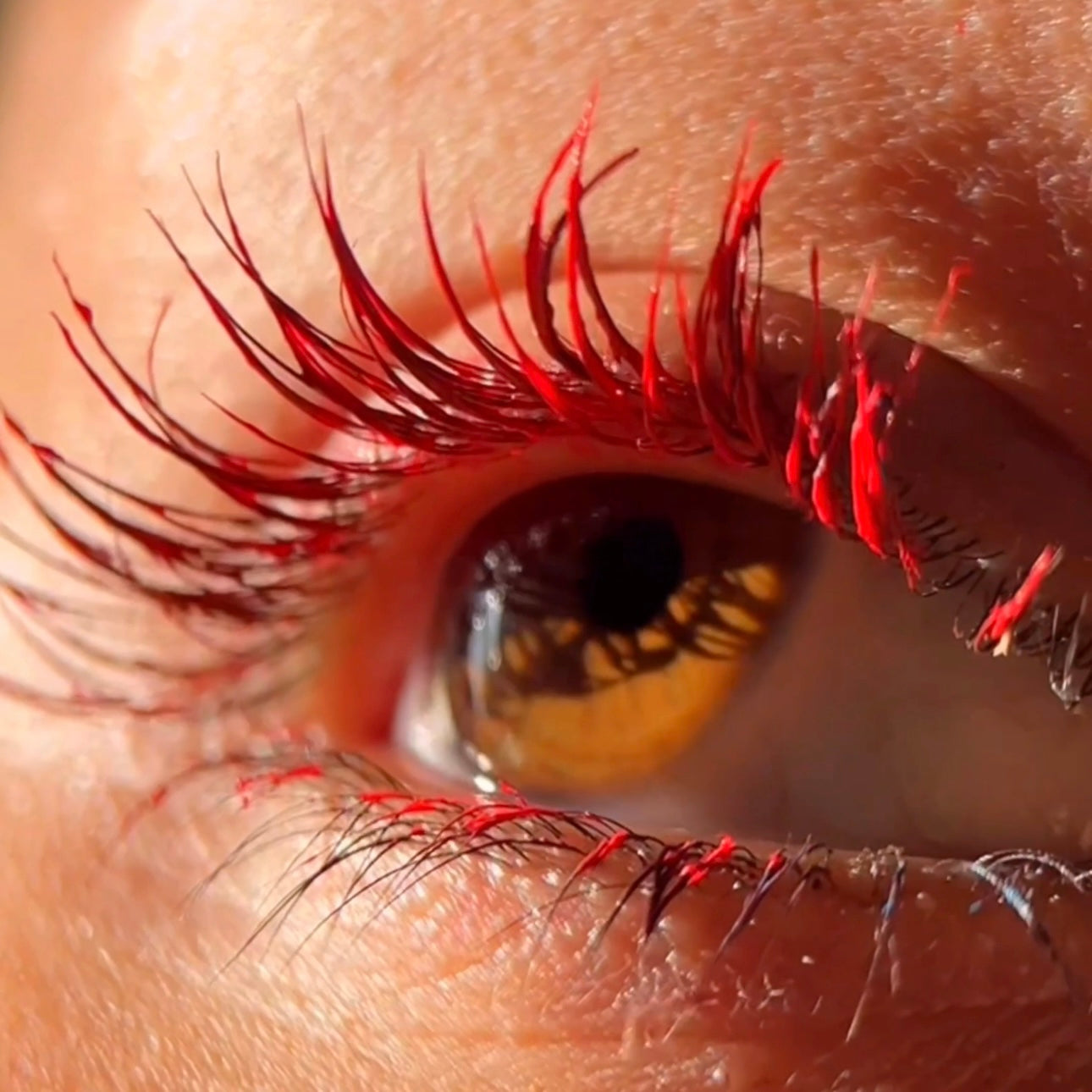 Close-up of a brown eye with lashes coated in red mascara.