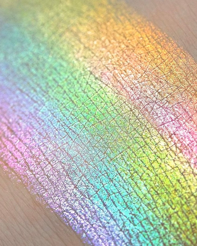Vibrant rainbow highlighter swatched on textured skin with visible iridescent shimmer.