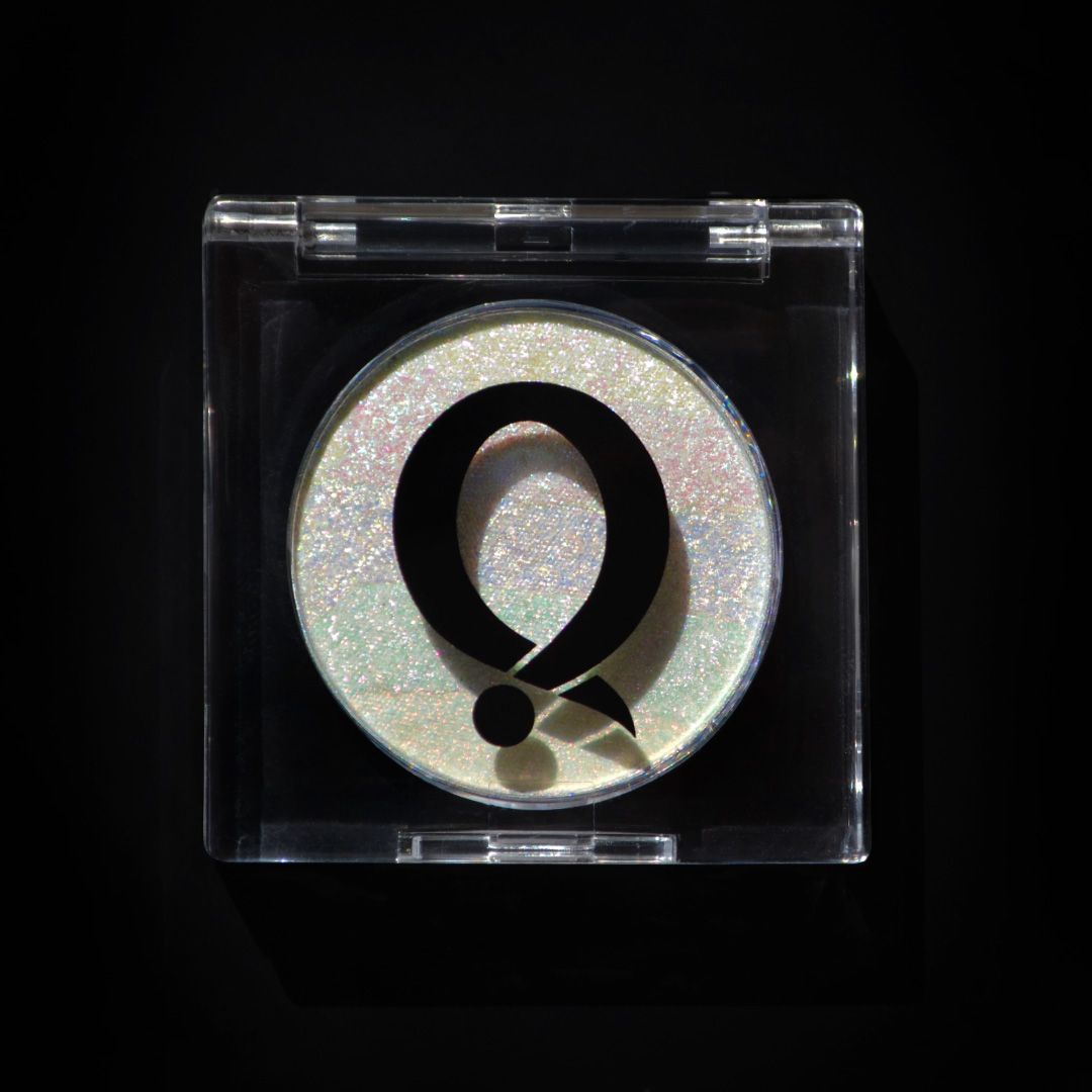 A highlighter with an iridescent finish is in a clear case featuring a bold black Q logo on the lid.