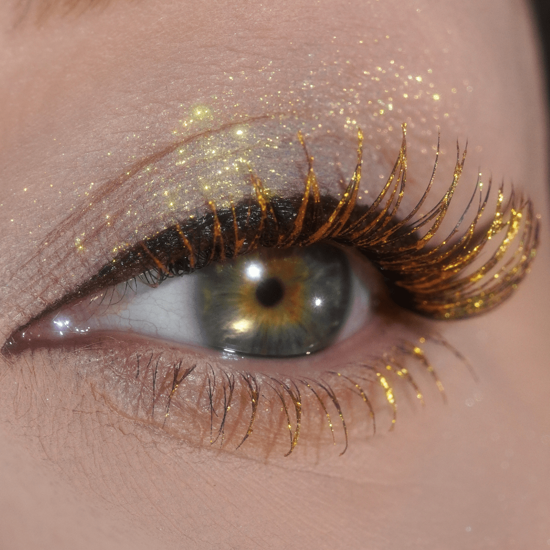 Close-up of a hazel eye with gold glitter on the lashes and eyelid