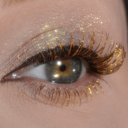 Close-up of a hazel eye with gold glitter on the lashes and eyelid