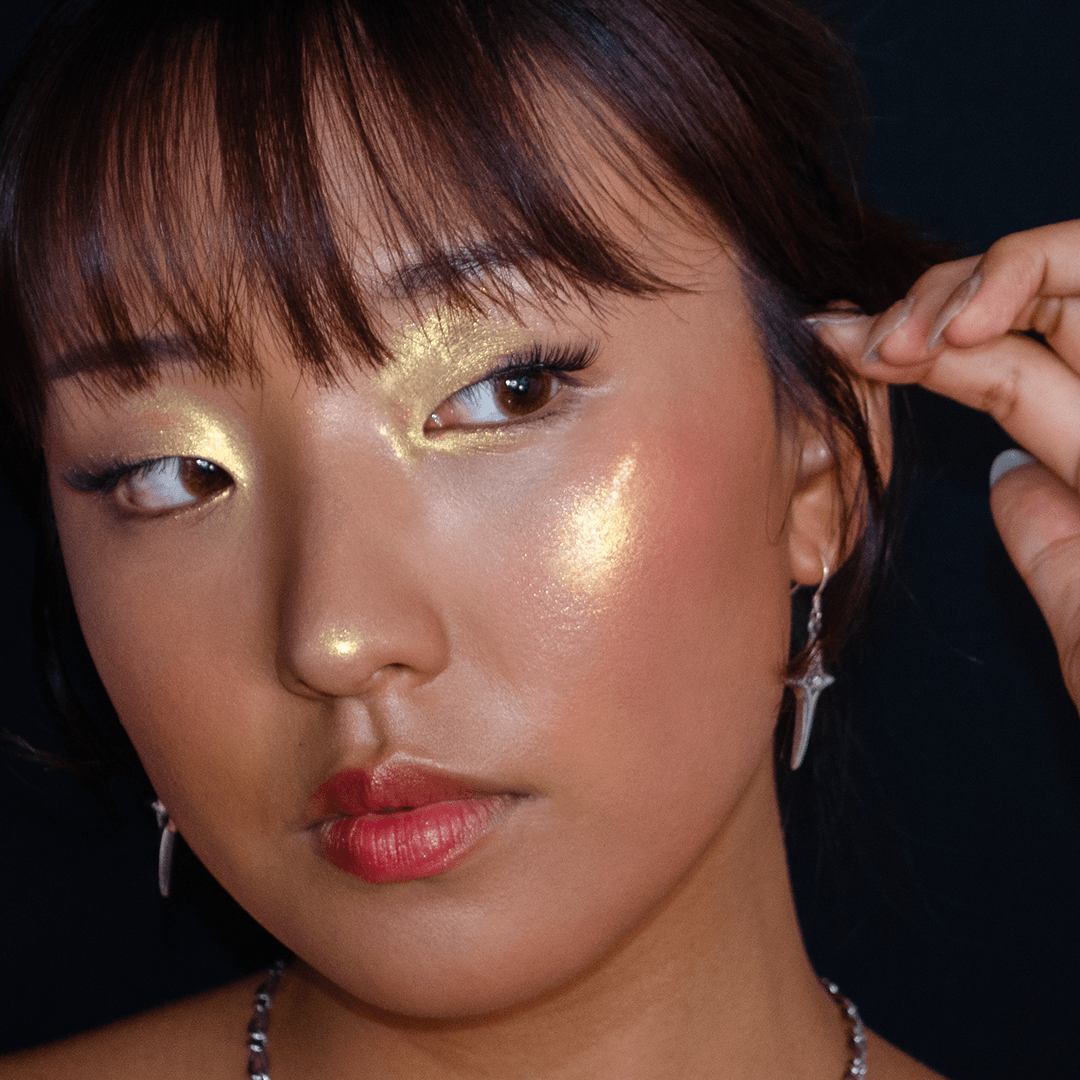 Woman with dewy skin and visible highlighter on her cheekbone wears silver jewelry.