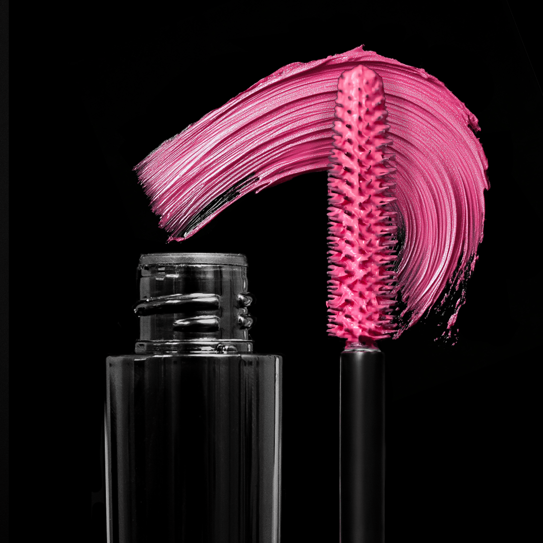 A black mascara tube and wand with bright pink mascara next to a bold pink swipe on a plain black background.