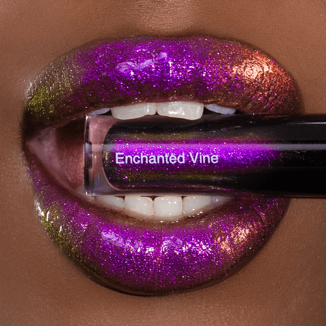 Lips with a glossy purple, pink, and gold shimmer finish are shown holding a lip gloss tube with logo Enchanted Vine.