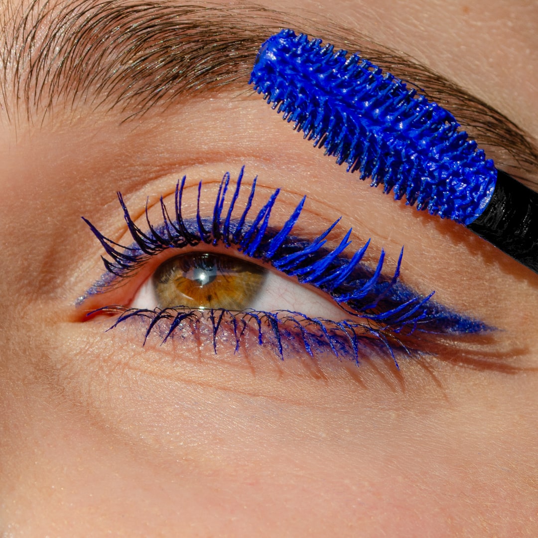 A close-up of long eyelashes being coated with mascara using a bright blue wand.