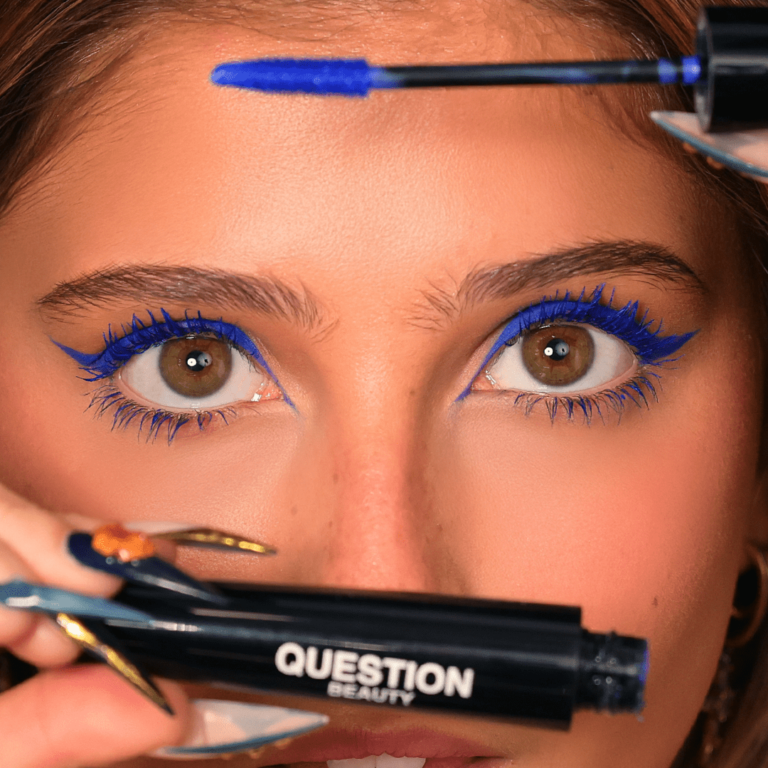 A woman with blue eyeliner and mascara holds a tube labeled Question Beauty