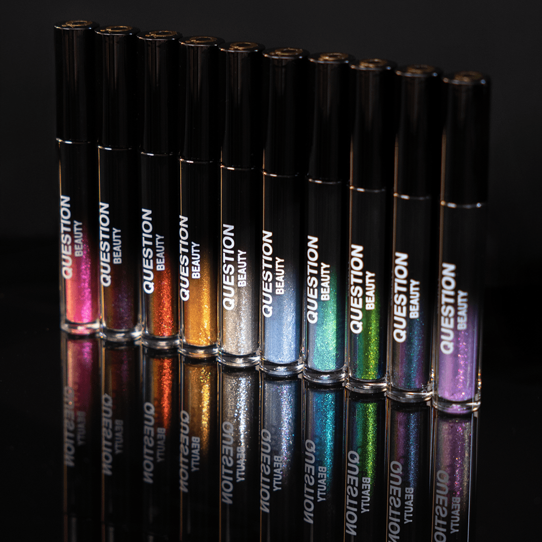 Ten mascara topper tubes in assorted colors are lined up neatly on a black surface.