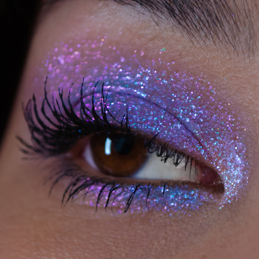 Close-up of an eye with long lashes wearing shimmery purple, blue, and pink glitter eyeshadow.