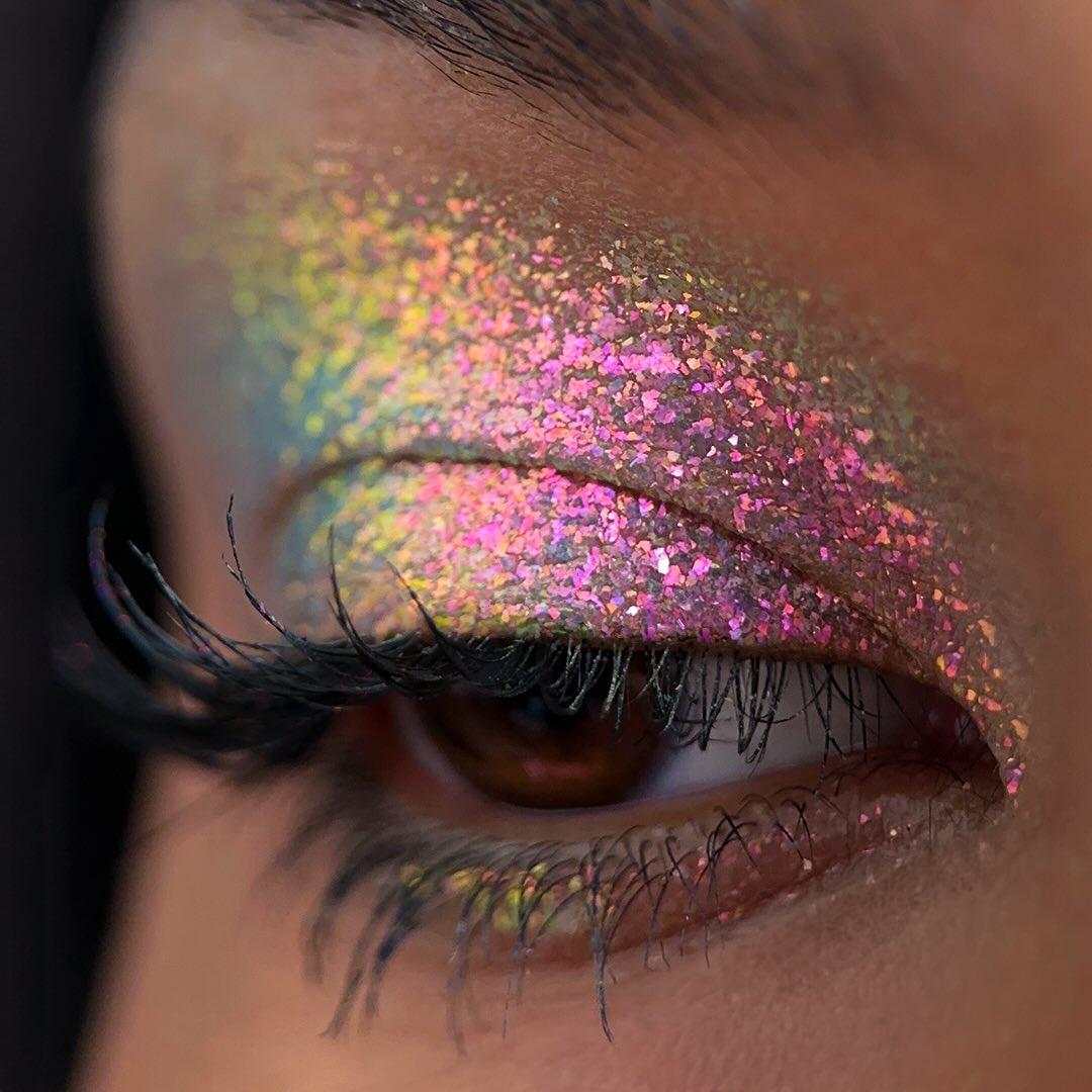 Close-up of an eye with pink and green glitter eyeshadow on the eyelid and long dark eyelashes.