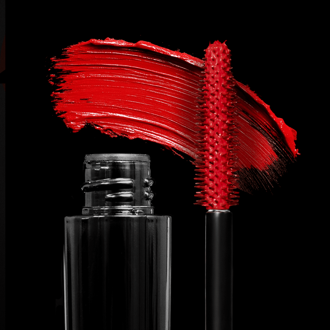 A mascara wand with cherry red product is shown against a black background.