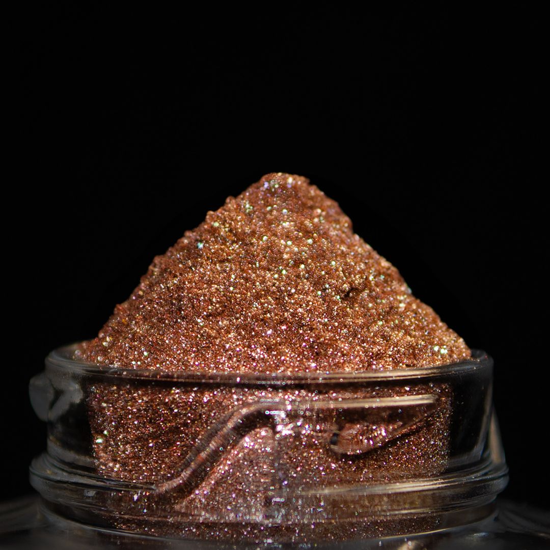 A small glass jar filled with coppery glitter and is shown against a black background.
