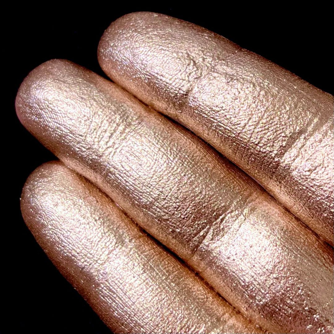 Three fingers coated in shiny metallic gold pigment against a black background.