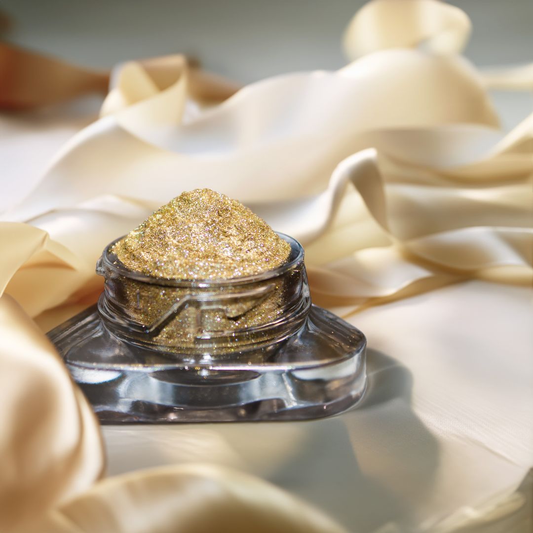 A small jar filled with gold glitter sits on cream-colored satin fabric.