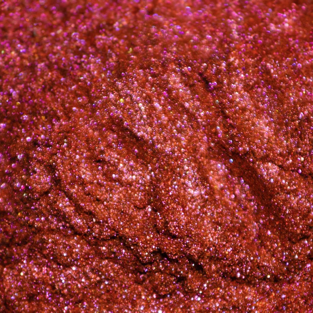 Close-up of a surface with red and pink holographic glitter creating a textured, sparkling appearance.