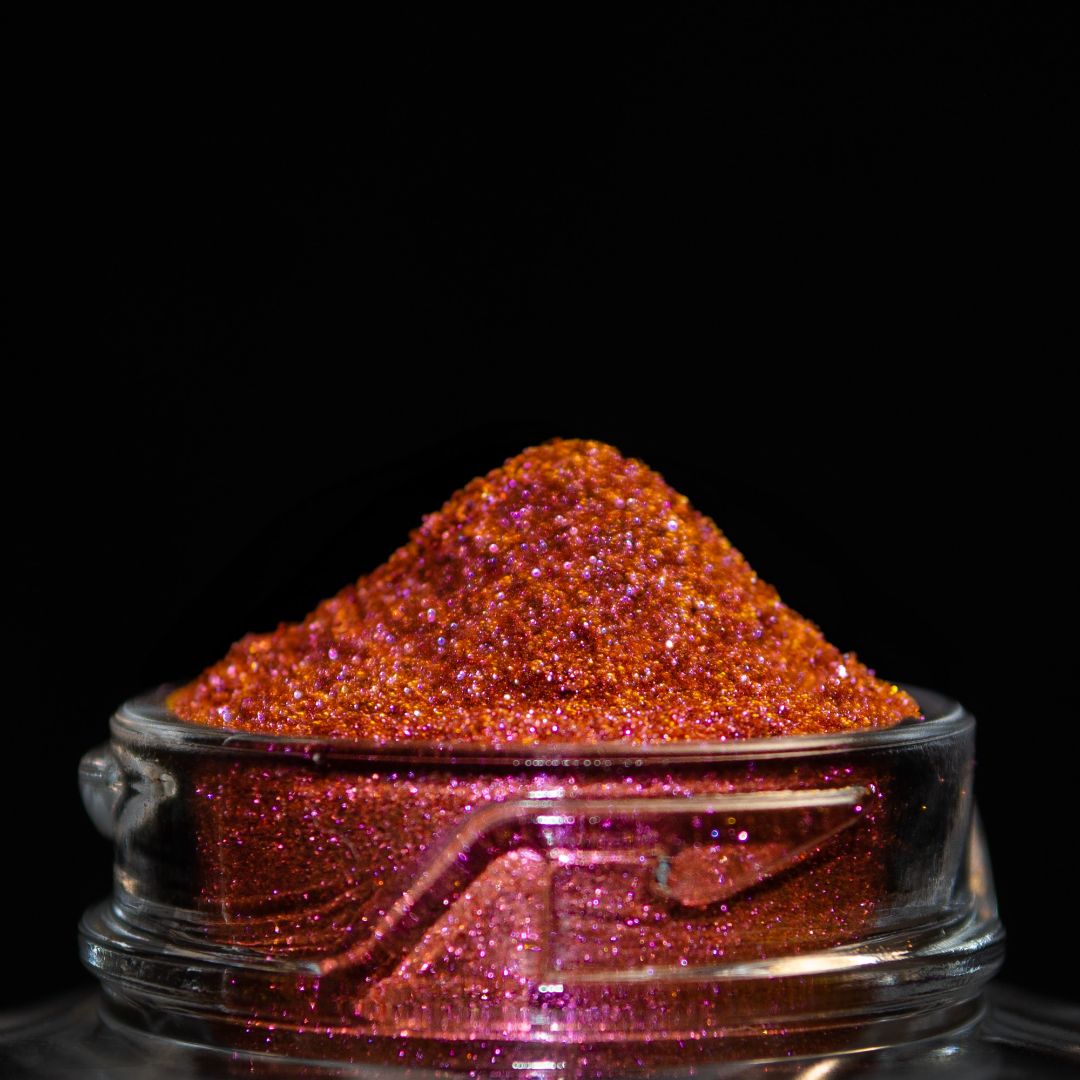 A close-up picture of a jar with orange and pink glitter against a black background.