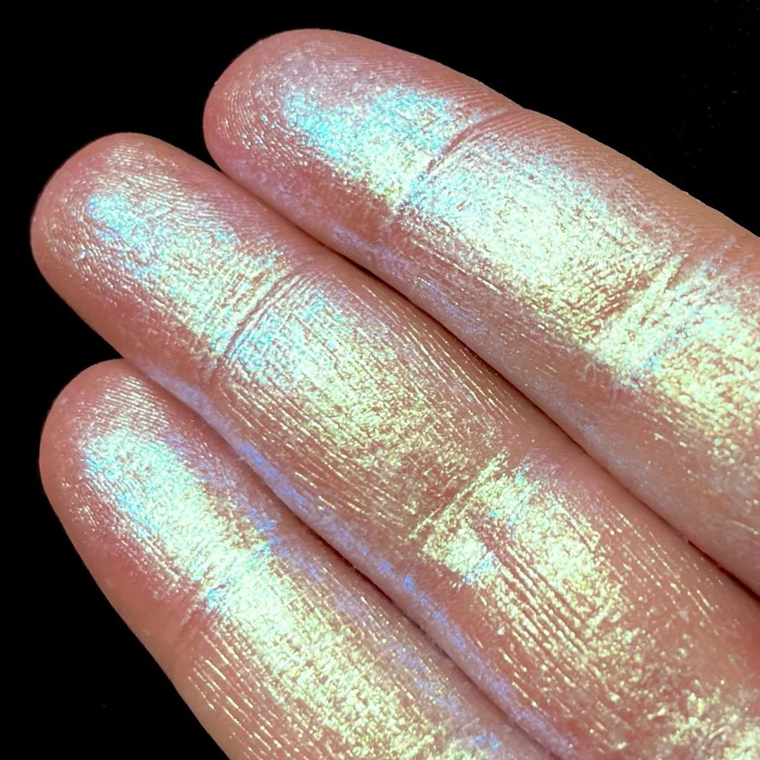 Close-up of fingers coated in iridescent shimmery pigment with a gold base and green and pink reflective tones