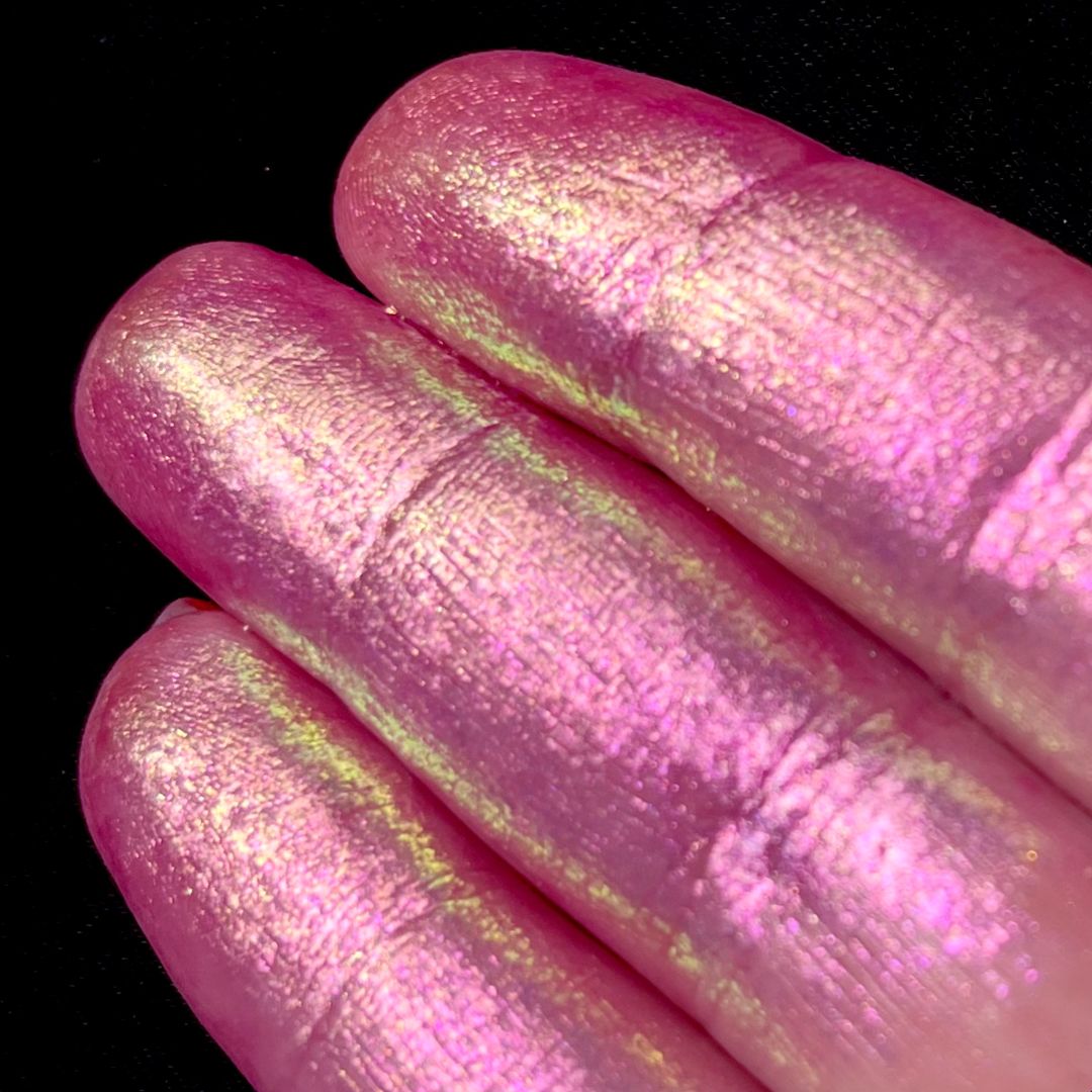 Three fingers display iridescent pastel pink pigment on their nails against a solid black background.
