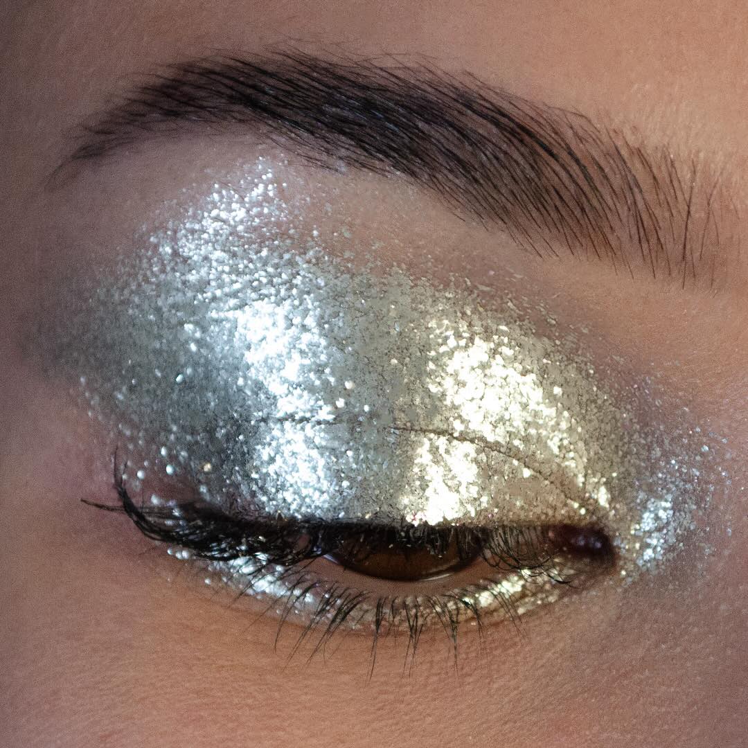Close-up of a closed eye with silver glitter eyeshadow and long thick false eyelashes.