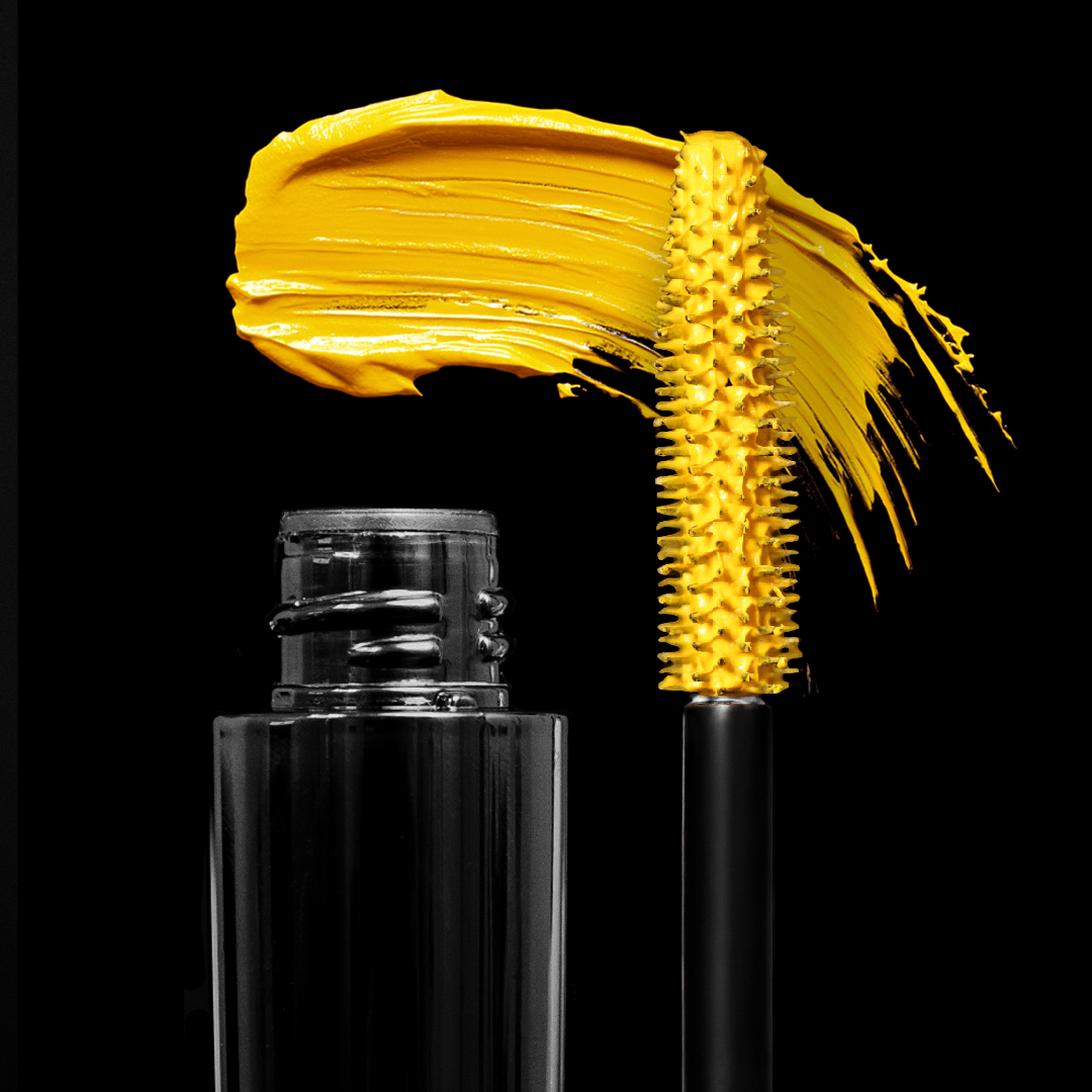 An open black mascara tube with a yellow brush and a bright streak of color on a black background.