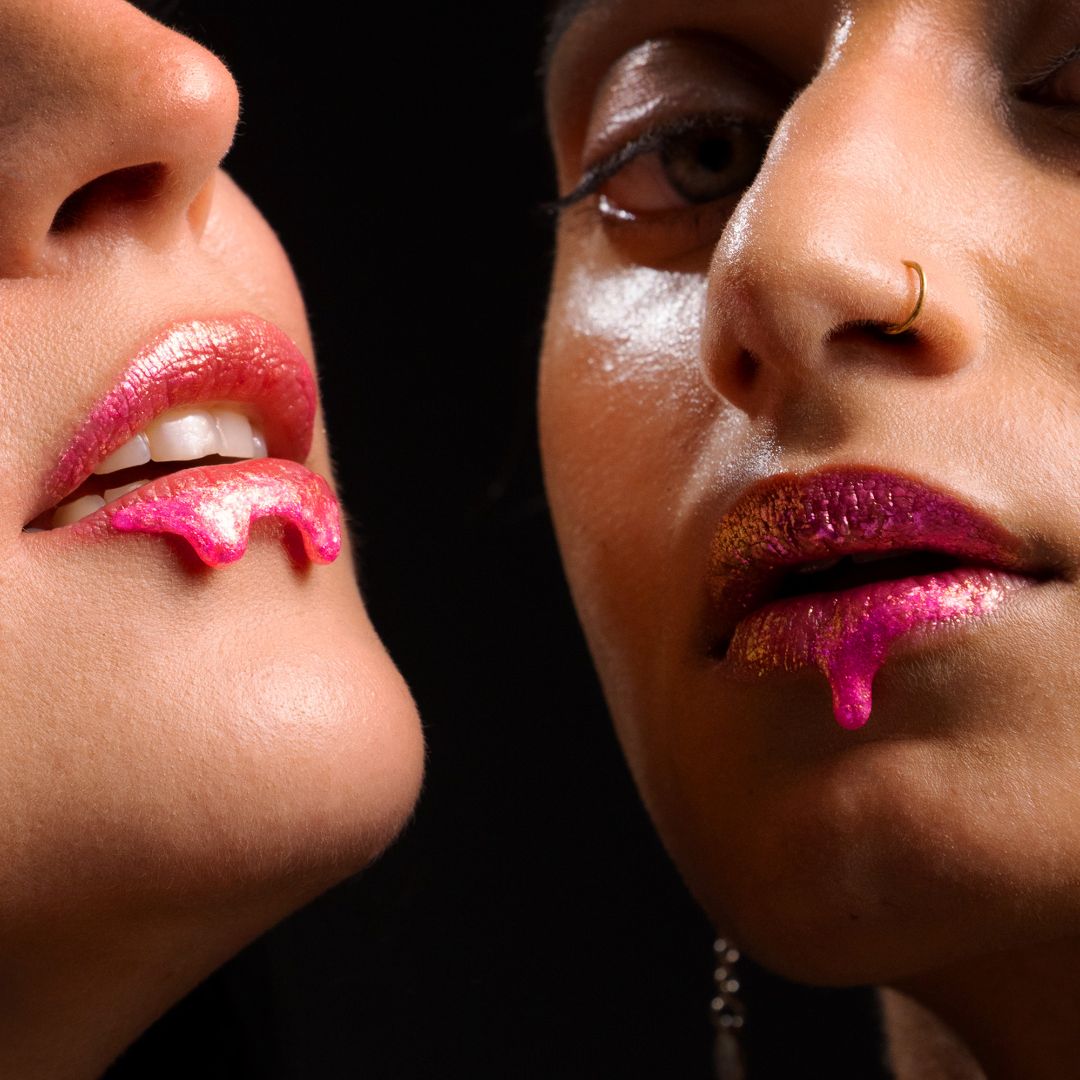 Two women with glossy magenta lips stand side by side in front of a dark background.