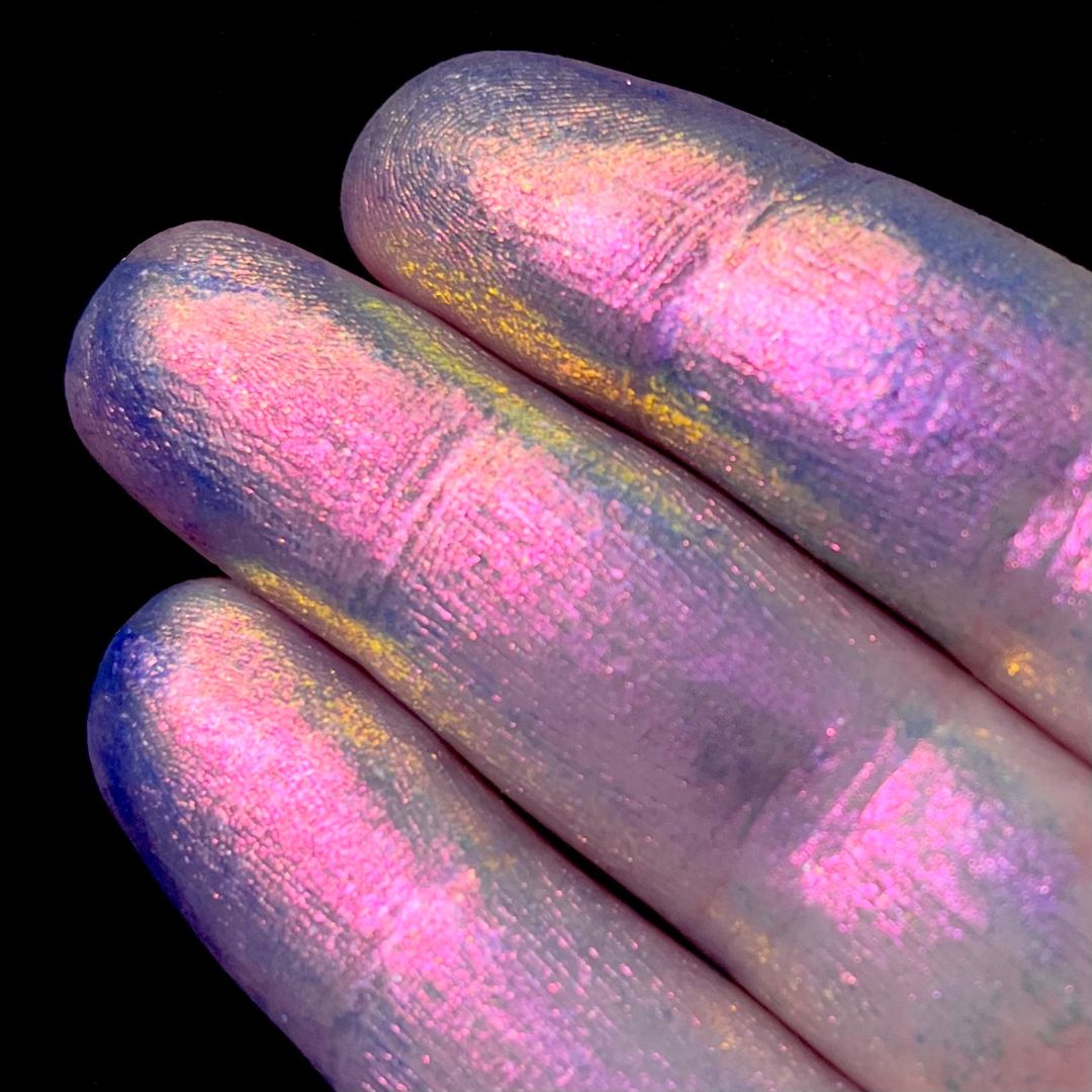 Close-up of three fingers painted with iridescent pink and purple glitter against a black background.