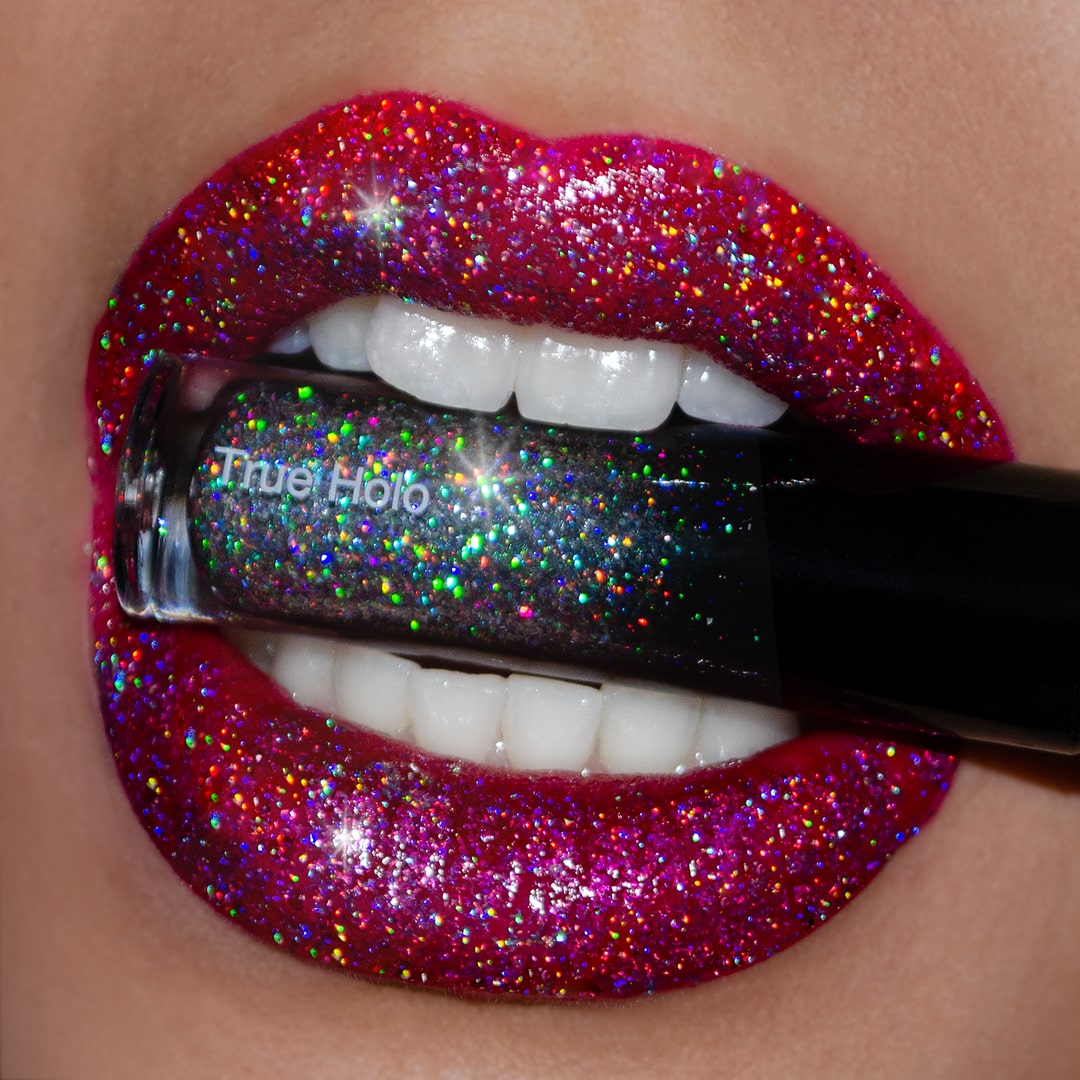 A pair of glittery red lips holds a True Holo tube with a holographic shine.