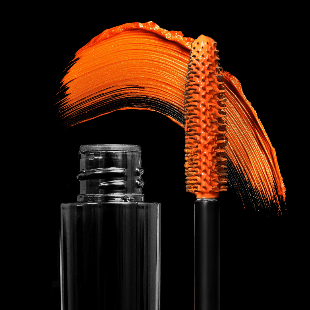 Black mascara tube and wand with orange mascara swiped in an arc on a black background.