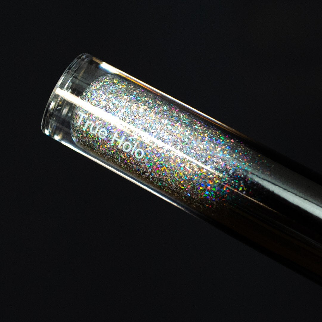 A clear tube of lip gloss with holographic glitter sits on a dark background.