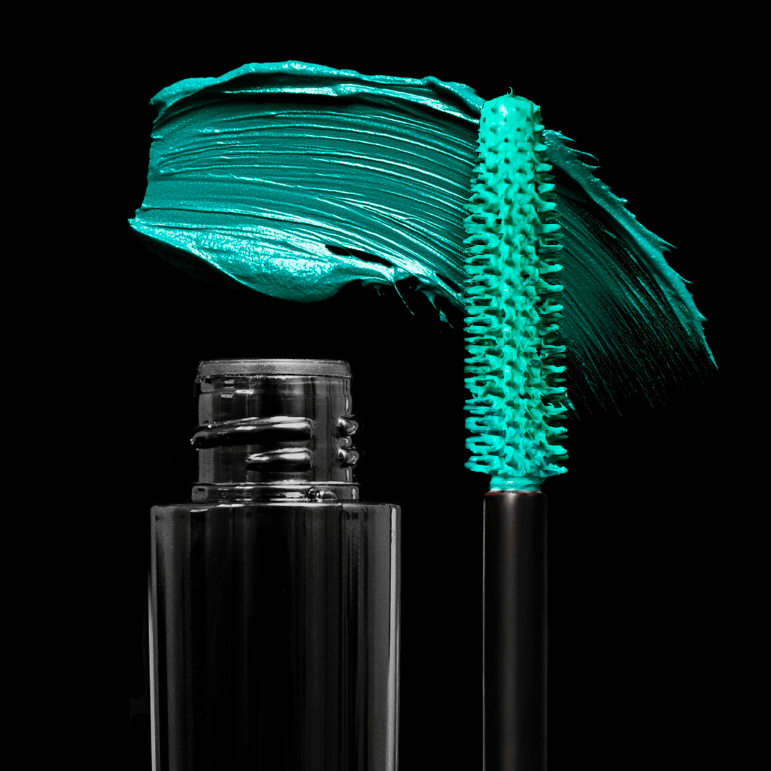 A black mascara tube and wand with bright turquoise mascara are shown against a black background.