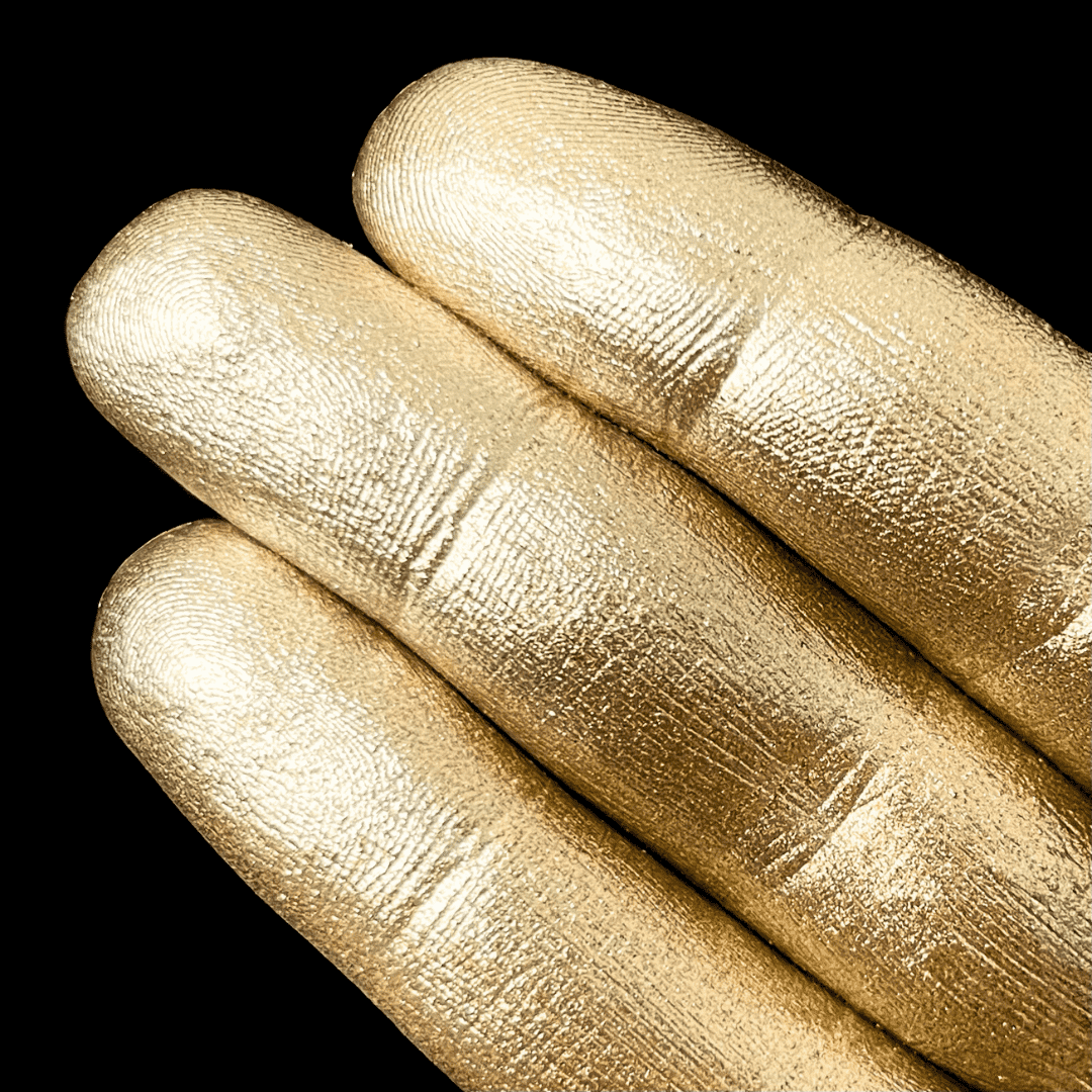 Three fingers display iridescent gold pigment on their nails against a solid black background.