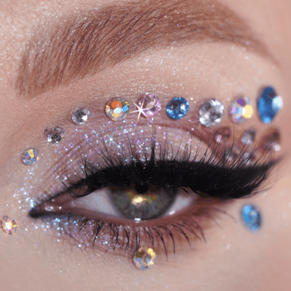 Close-up of an eye with glitter eyeshadow, dramatic lashes, black eyeliner and self-adhesive iridescent gems on the eyelid.